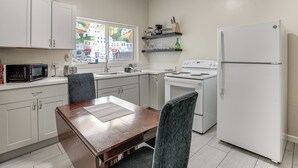 A kitchen with white cabinets, a dining table, chairs, a refrigerator, and a window with a view of buildings. - Walkable Dtwn Oakland Apt w/ Shared Rooftop! (Oakland)