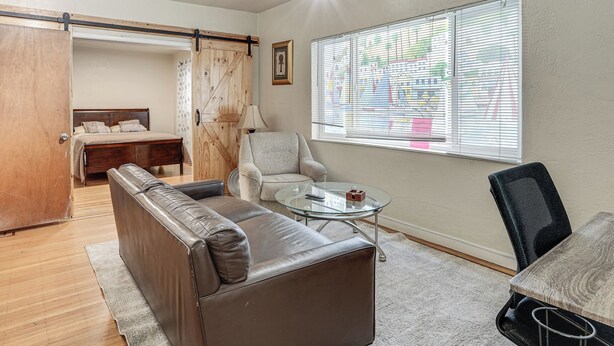 A room with a bed, a sofa, a chair, a small table, and a window with blinds. - Walkable Dtwn Oakland Apt w/ Shared Rooftop! (Oakland)