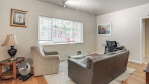 A living room with a sofa, a glass coffee table, a lamp, a fan, and a window with blinds. - Walkable Dtwn Oakland Apt w/ Shared Rooftop! (Oakland)