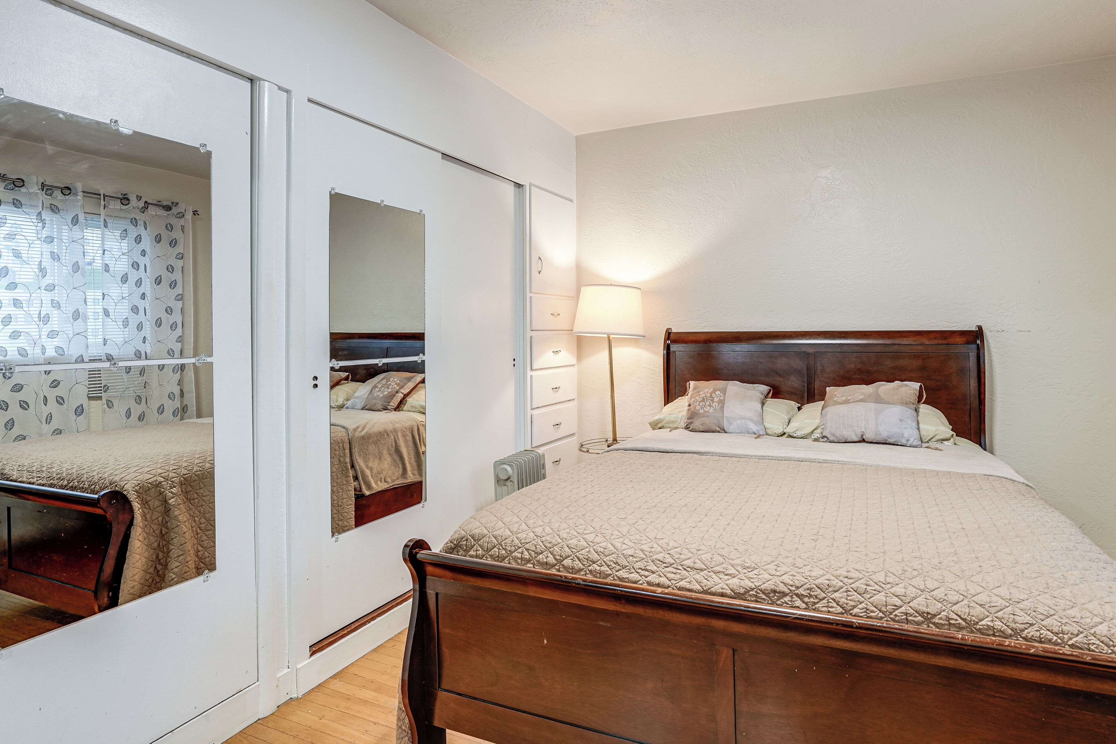 A bedroom with a wooden bed, a mirror, a bedside lamp, and a window with a curtain.