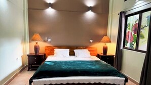 Un lit recouvert d’une couvre-lit de couleur turquoise, deux lampes de chevet et une œuvre d’art florale encadrée accrochée au mur.