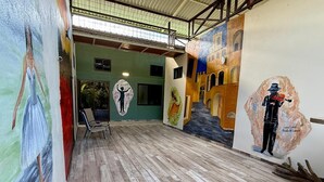 Une pièce avec un plancher en bois, une fresque représentant une figure tenant un enfant, et une chaise.
