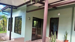 Un espace extérieur abrité, doté d’un sol en béton, de plantes en pot et d’une porte donnant accès à un espace intérieur.