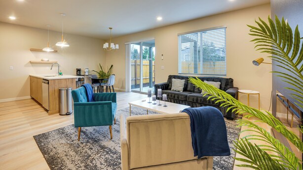 Een moderne woonkamer met een bank, stoelen, een salontafel en een keukenhoek met een spoelbak en aanrecht.