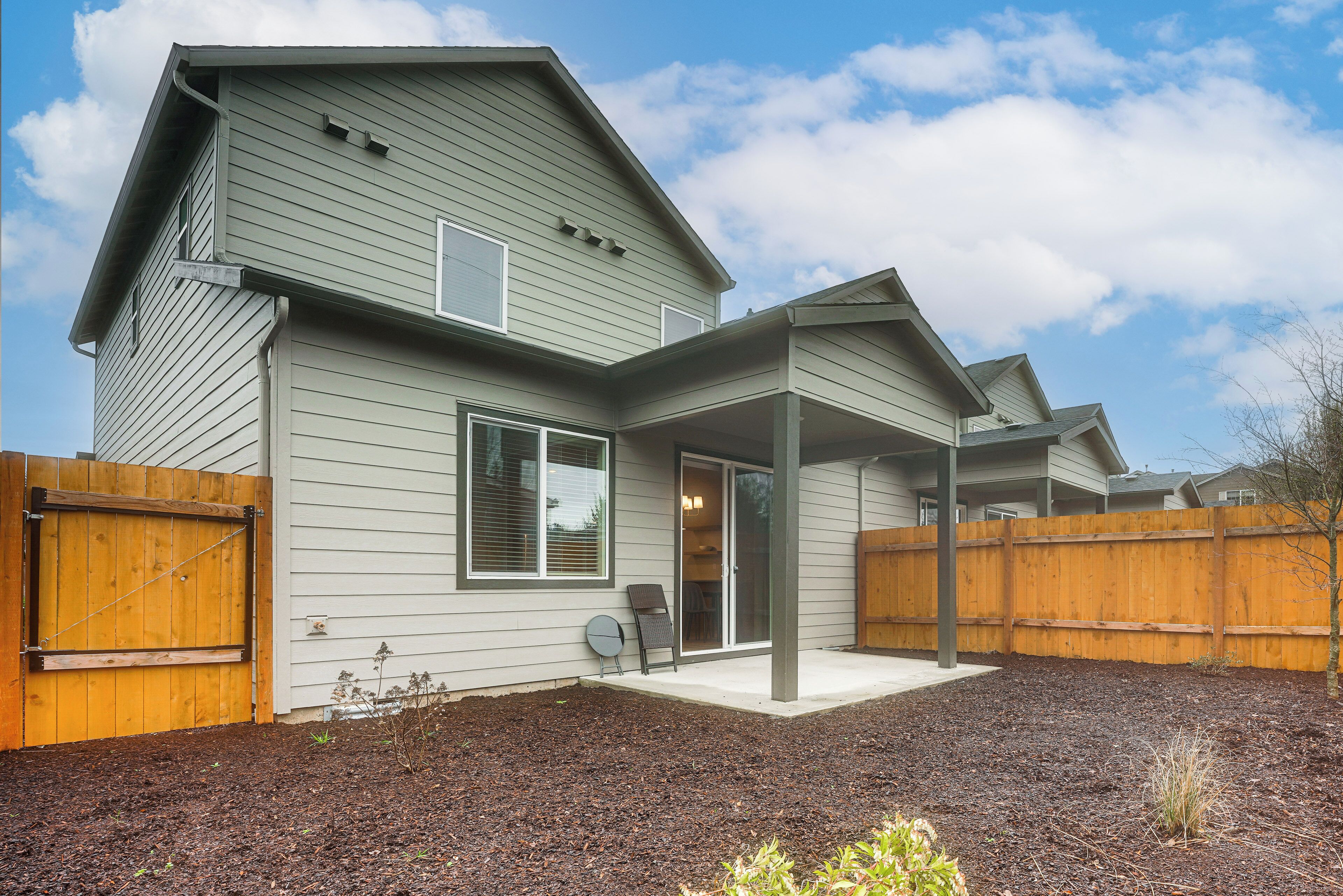 A two-story house with a covered patio, a wooden fence, and a landscaped backyard.