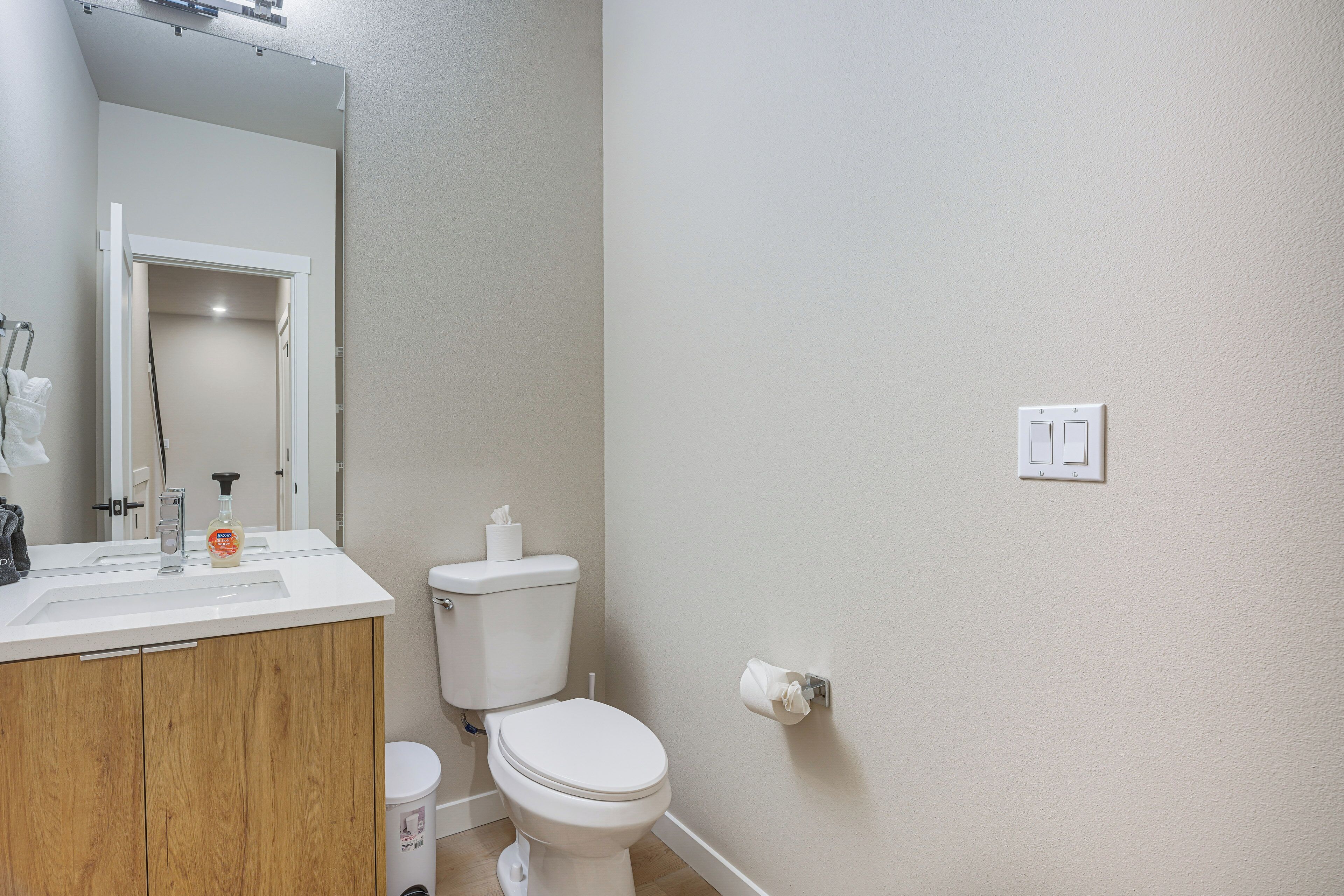 A bathroom with a wooden vanity, a toilet, a mirror, and a wall-mounted light switch.