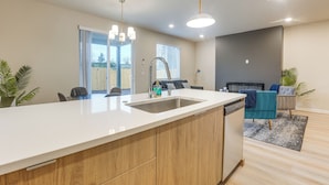 Een moderne keuken met een groot eiland, een inbouwvaatwasser en een eethoek met een blauwe stoel en een grijze bank.