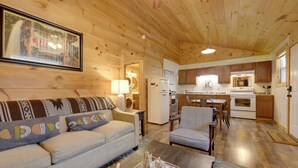A cozy cabin interior with a sofa, chairs, a dining table, a kitchen area, and a framed picture on the wall. - Cozy Cabin By Gsmnp! Soaking Tub, Views + Fire Pit (Cosby)