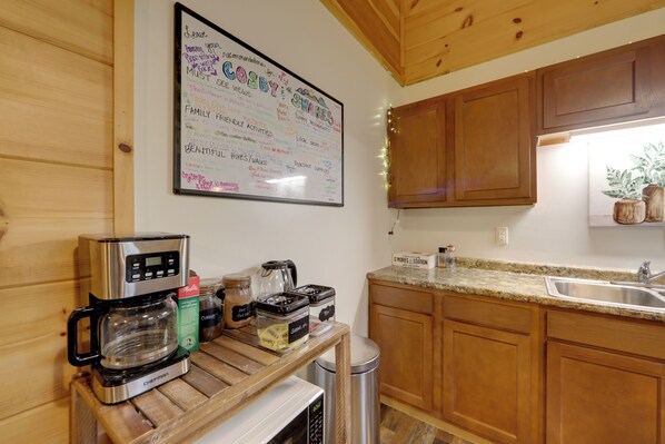 Una cocina con armarios de madera, cafetera, microondas y pileta de acero inoxidable.