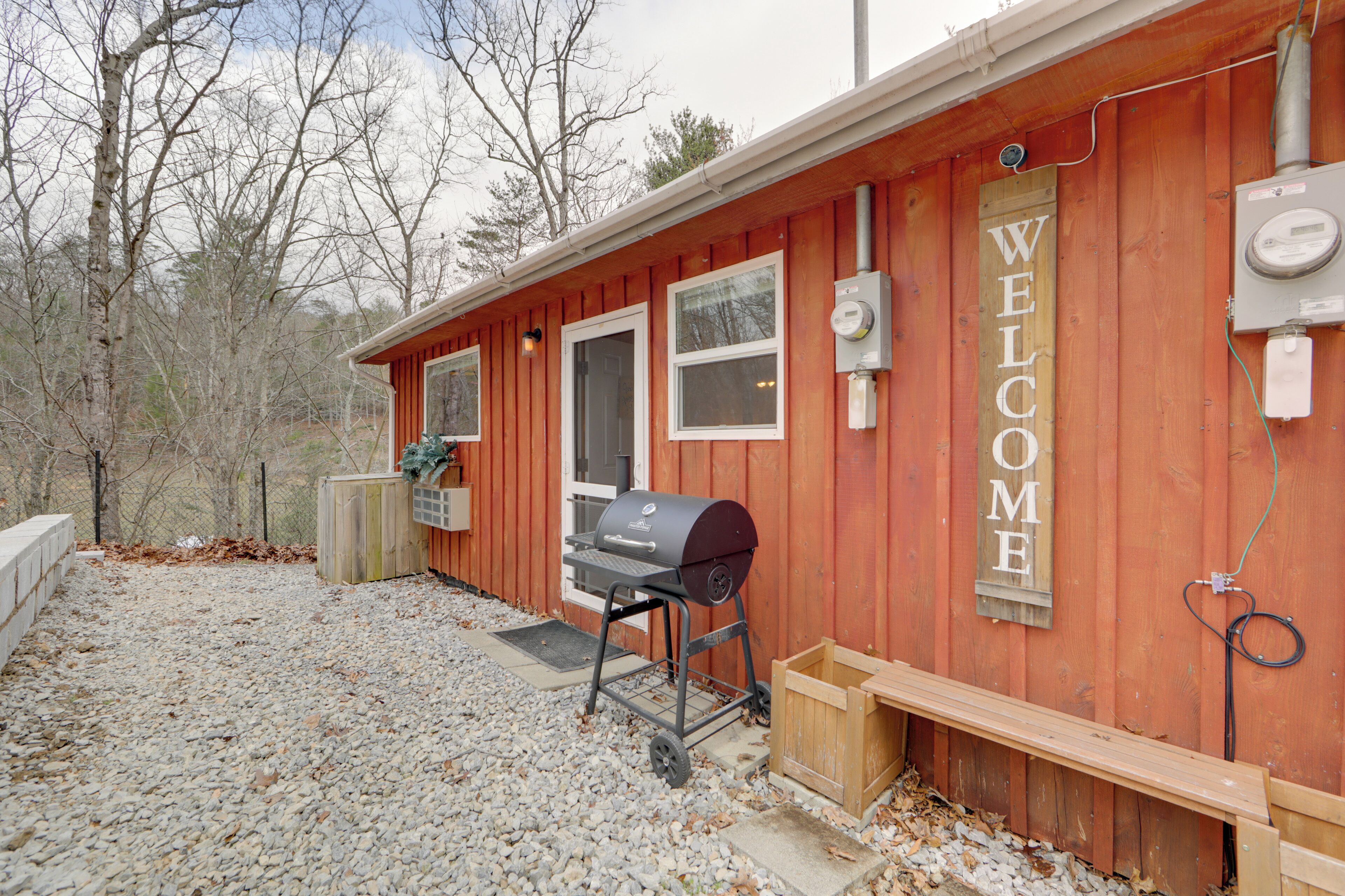 A wooden building with a 'WELCOME' sign, a barbecue grill, and a wooden bench.