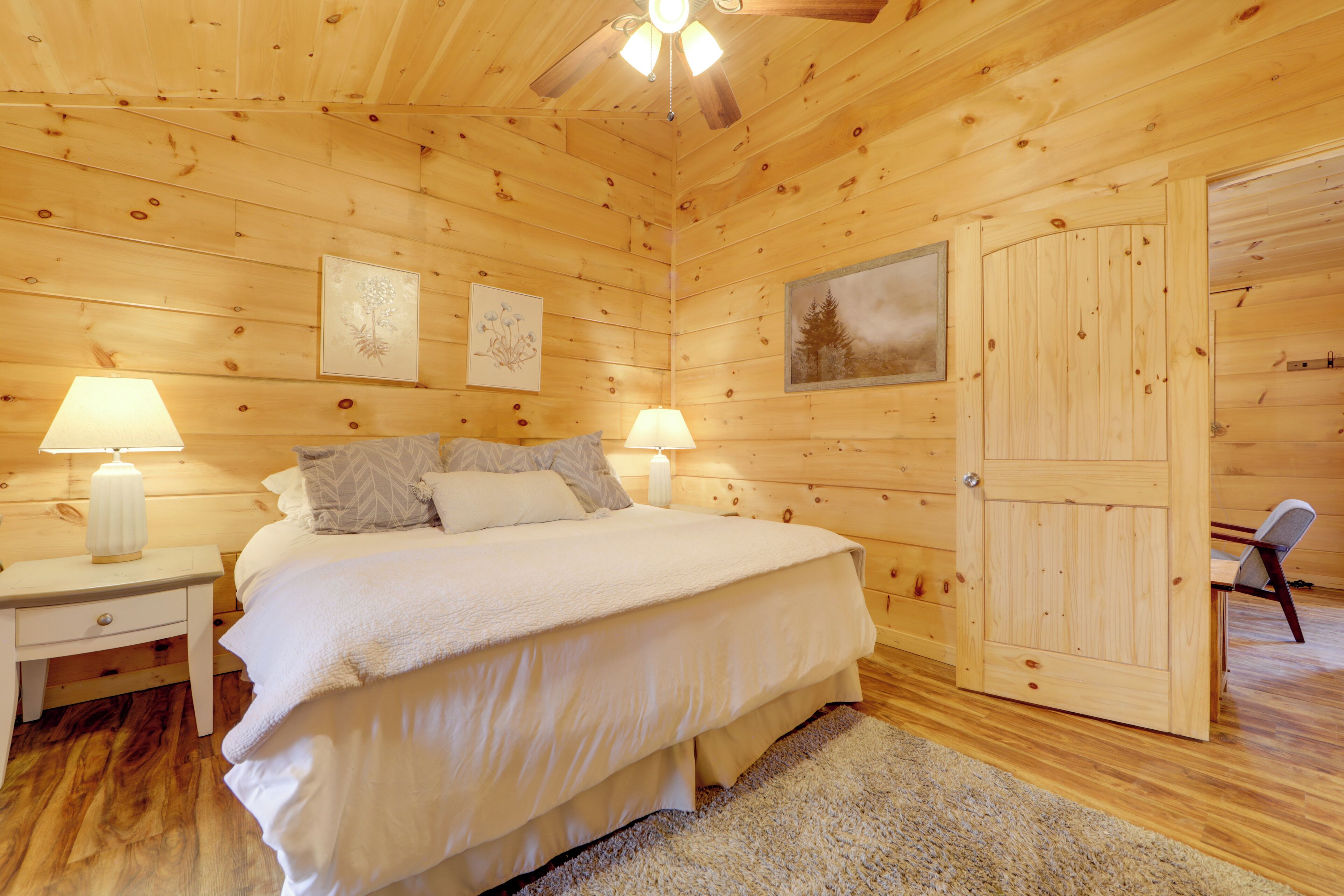 Een slaapkamer in een houten blokhut met een bed, twee nachtkastjes, een deur en een stoel.