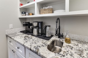 A kitchen with a granite countertop, a coffee maker, a kettle, a sink, and a soap dispenser.