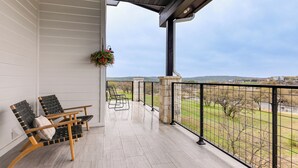 A balcony with two chairs, a hanging planter, and a view of a green landscape. - Hot Tub, Lake View! Lakefront Marble Falls Home (Marble Falls)