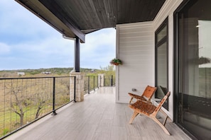 A balcony with a wooden floor, a chair, a hanging flower basket, and a view of trees and buildings.