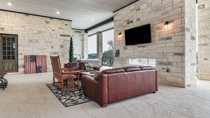 A spacious living area with a stone wall, leather sofa, and a flat-screen TV mounted on the wall. - Hot Tub, Lake View! Lakefront Marble Falls Home (Marble Falls)