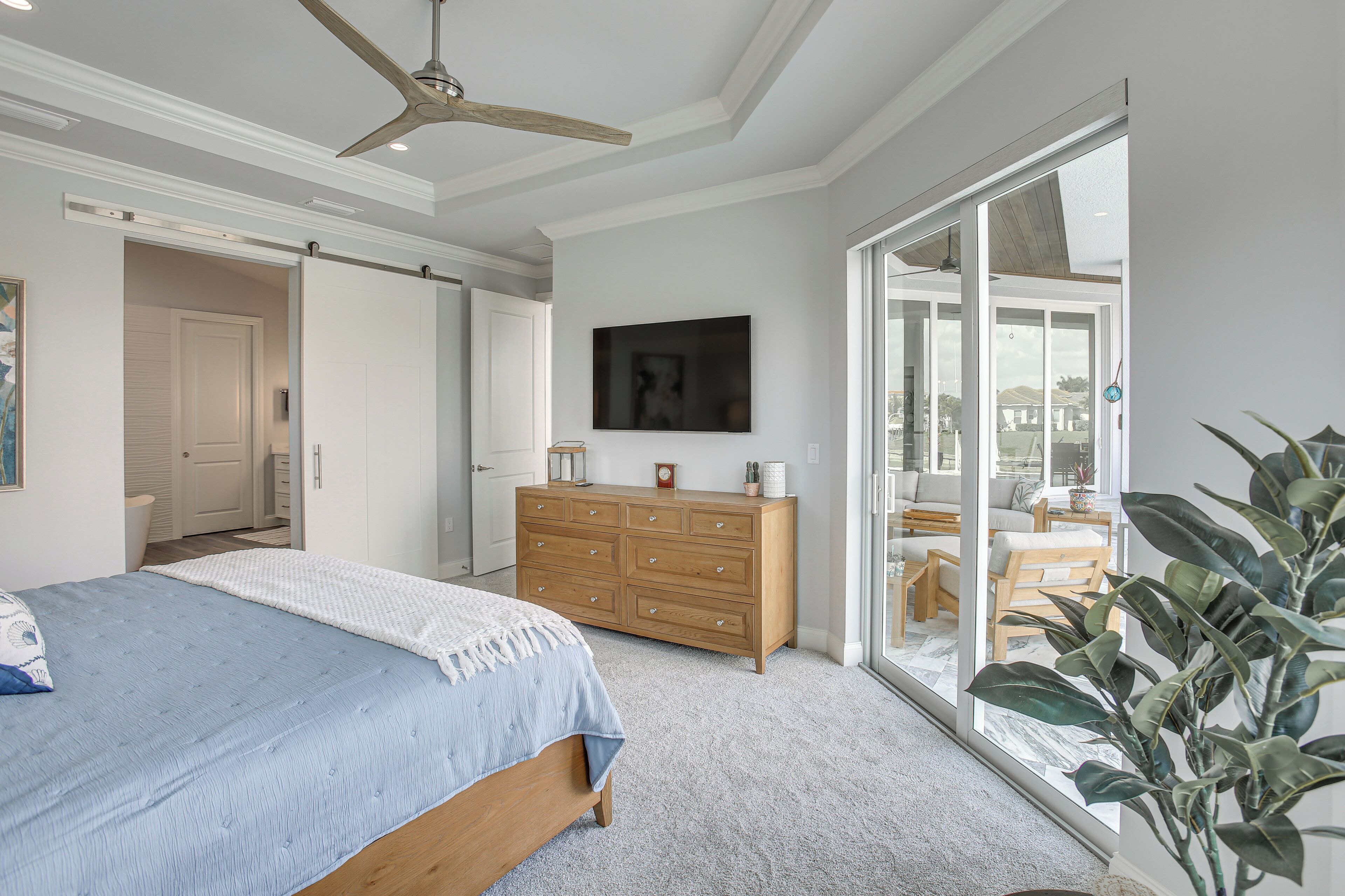 Ein Schlafzimmer mit einem Bett, einem Schminktisch, einem Deckenventilator und einer Glastür zum Balkon.