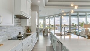 A modern kitchen with white cabinetry, a large island, and a view of a swimming pool. - Luxe Canal-front Getaway w/ Pool in Punta Gorda! (Punta Gorda)