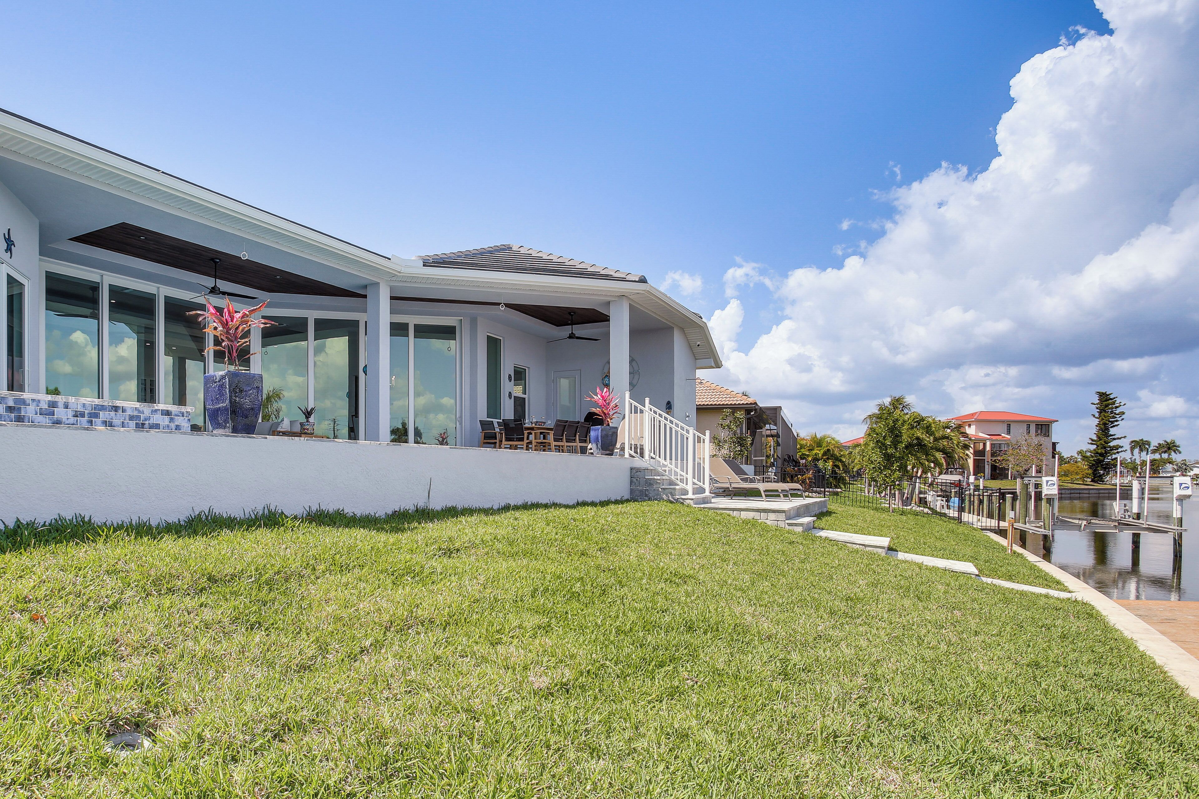 A modern house with large windows, a covered patio, and a grassy lawn.