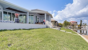 A modern house with large windows, a covered patio, and a grassy lawn. - Luxe Canal-front Getaway w/ Pool in Punta Gorda! (Punta Gorda)