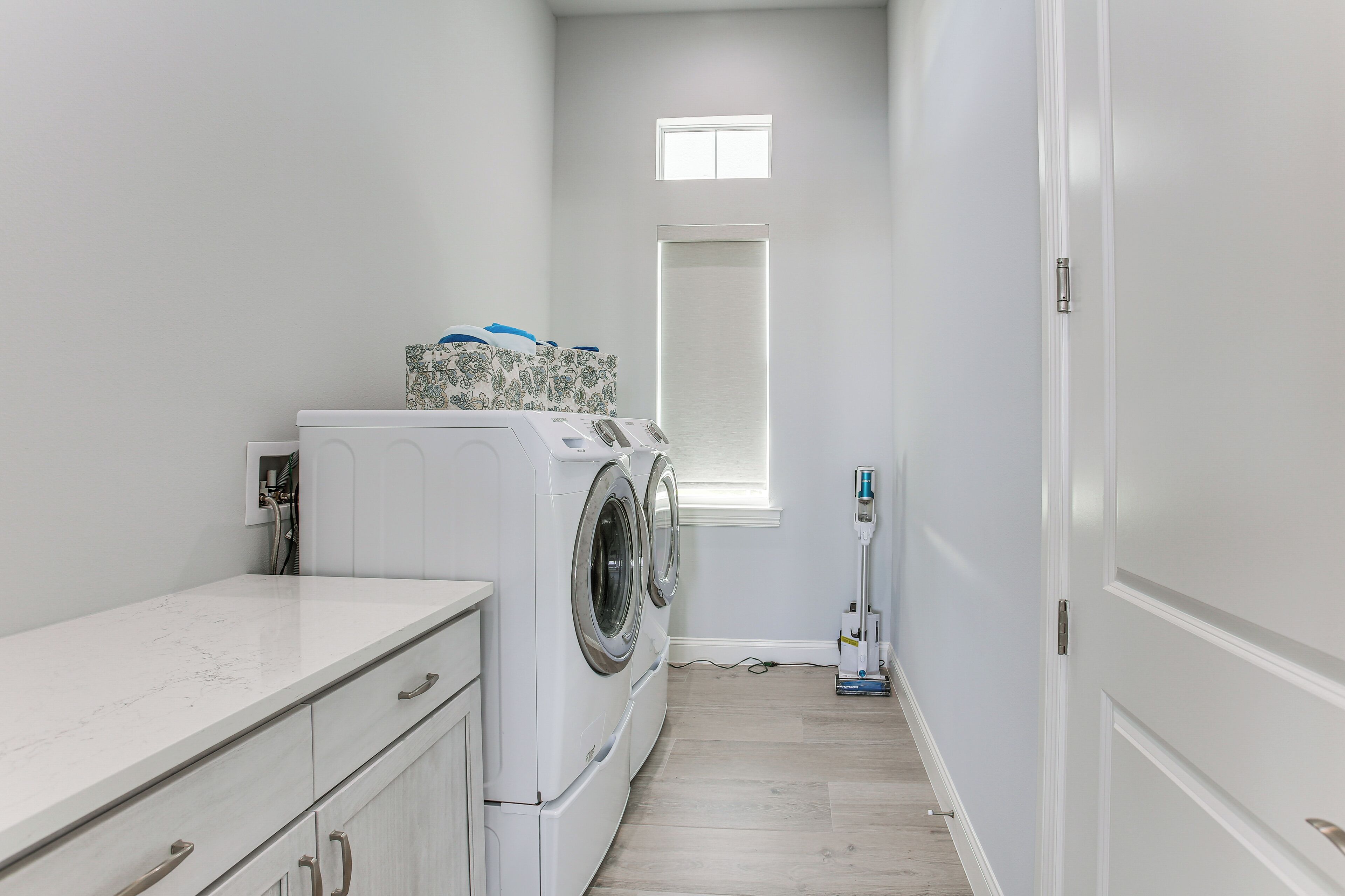 A laundry room with a washing machine, a dryer, a window, and a vacuum cleaner.