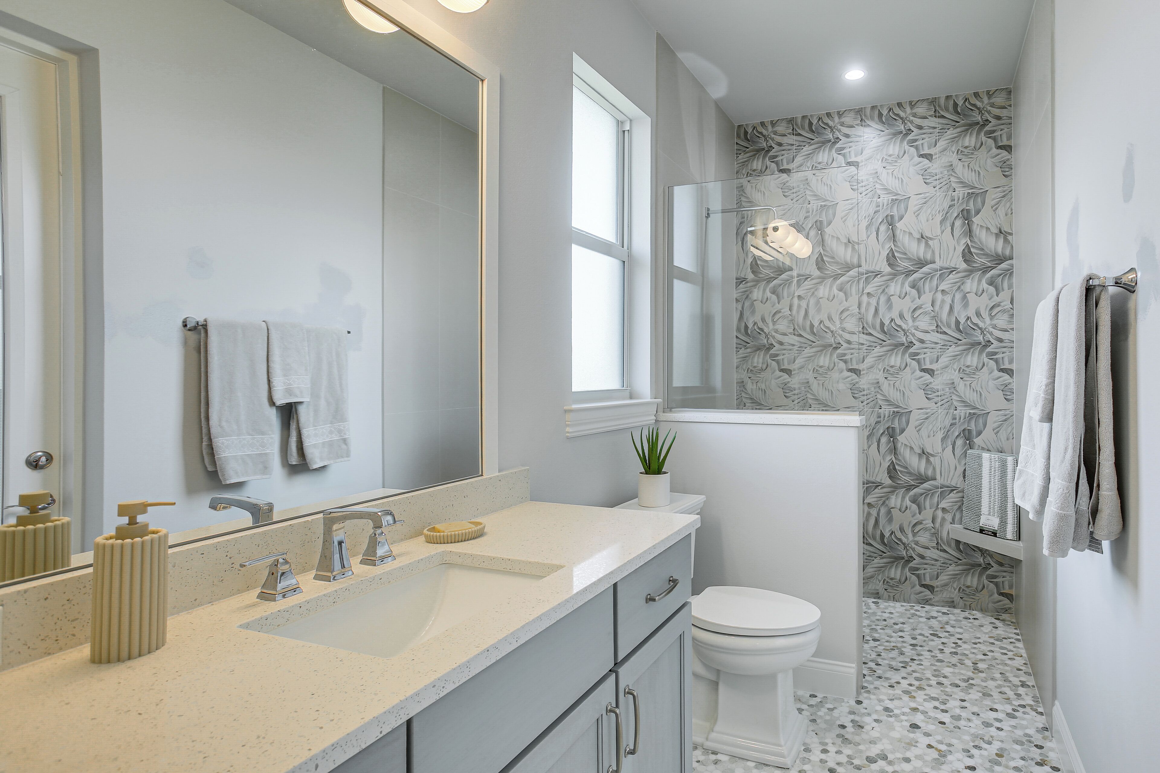 Un bagno con lavandino bianco, specchio, WC, zona doccia e rivestimento a motivi decorativi.