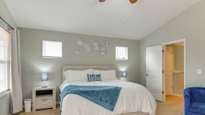 Un dormitorio con una cama, mesitas de noche, una silla azul y una puerta que da a otra habitación.