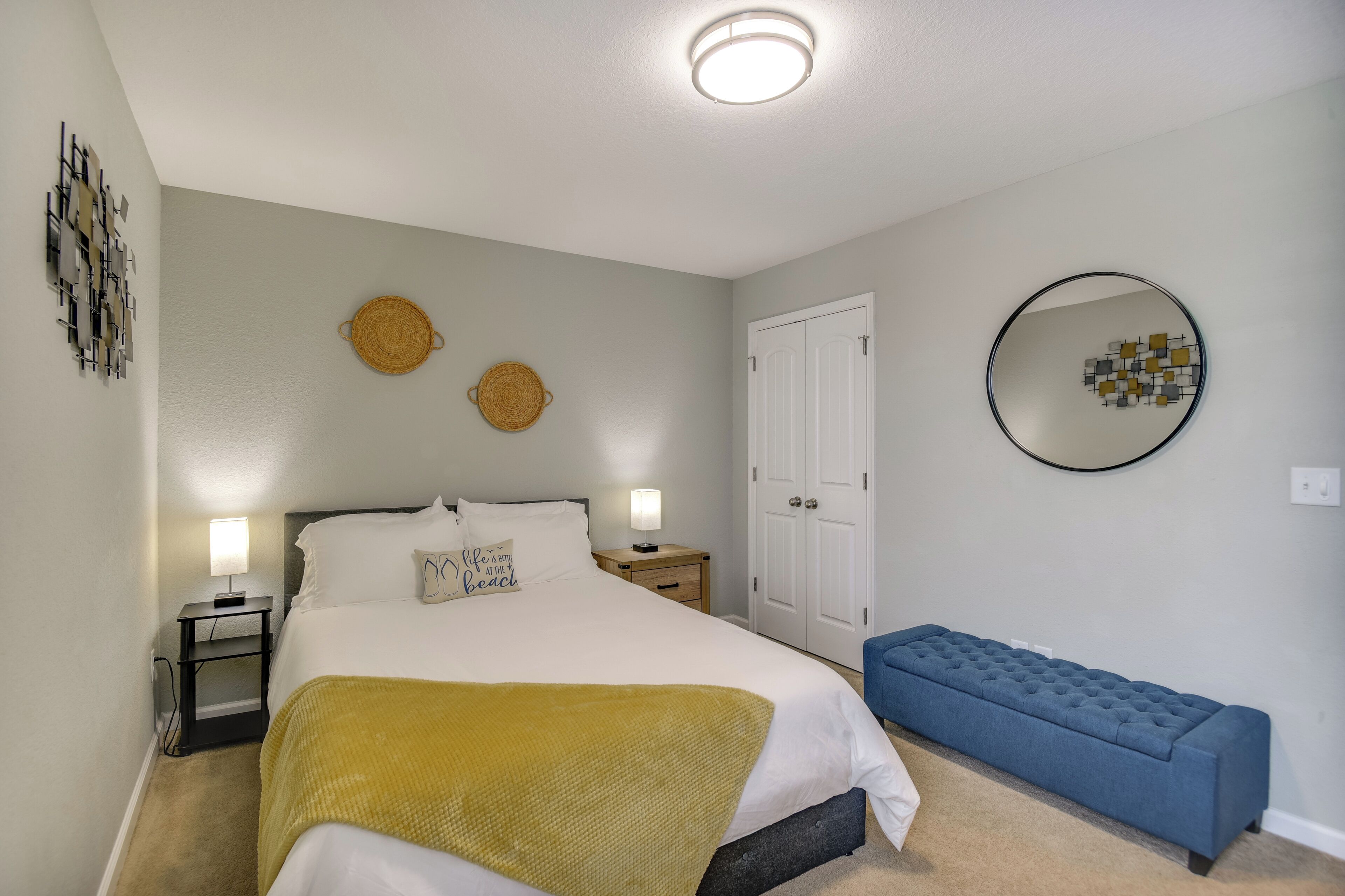A bedroom with a bed, bedside tables, a bench, a wall-mounted mirror, and a door.