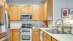 Eine Küche mit Holzschränken, Edelstahlgeräten, einer Mikrowelle, einem Backofen, einer Spüle und einem gemusterten Teppich.