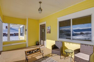 A yellow room with a bench, two wicker chairs, a small table, and a large window with a view of a snowy landscape.