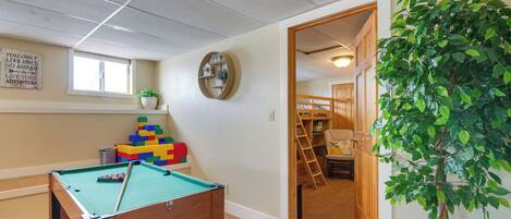 A pool table in a room with a window, a plant, and a wooden door leading to another room.