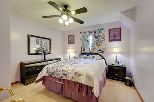 Un dormitorio con cama, ventilador de techo, cómoda, dos mesitas de noche con lámparas y una ventana con cortinas florales.
