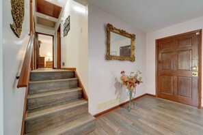 Eine Treppe führt zu einer zweiten Etage, eine Holztür, ein an der Wand befestigter Spiegel und eine Vase mit Blumen.