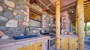A stone and wood kitchen with a built-in stove, sink, and cabinets. - Group Retreat on Flower Farm Near Sedona Trails (Cornville)