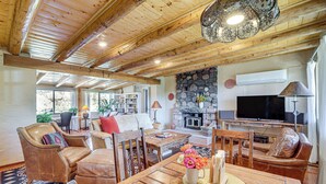 A spacious living area with a wooden ceiling, a stone fireplace, a television, and a dining table with a vase of flowers. - Group Retreat on Flower Farm Near Sedona Trails (Cornville)
