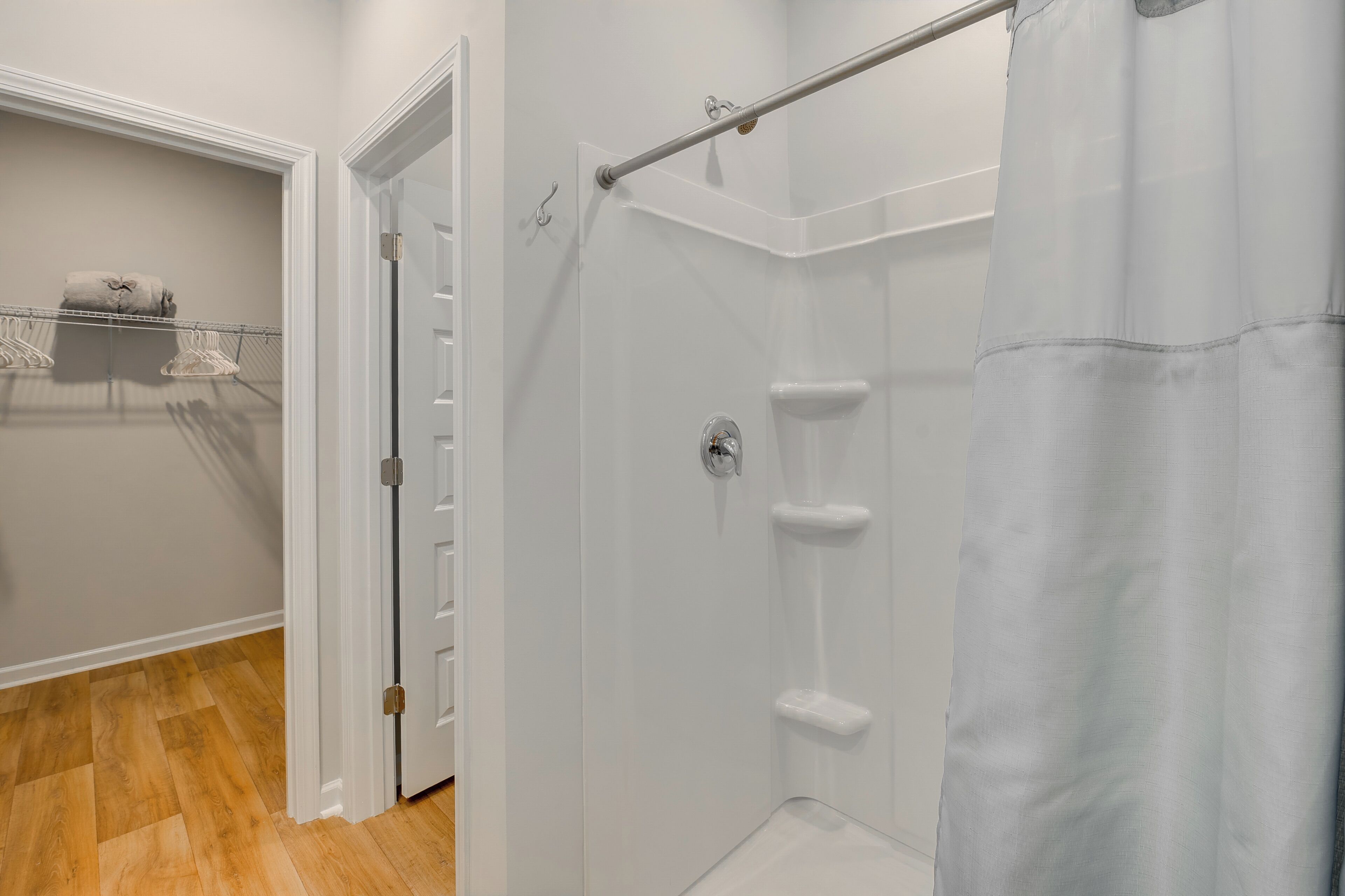 A bathroom with a shower, a towel rack, and a door leading to a closet.