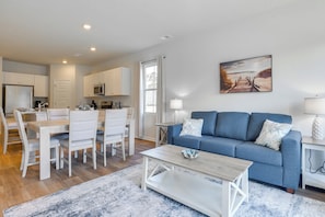 A modern living room with a blue sofa, white dining set, and a painting on the wall.