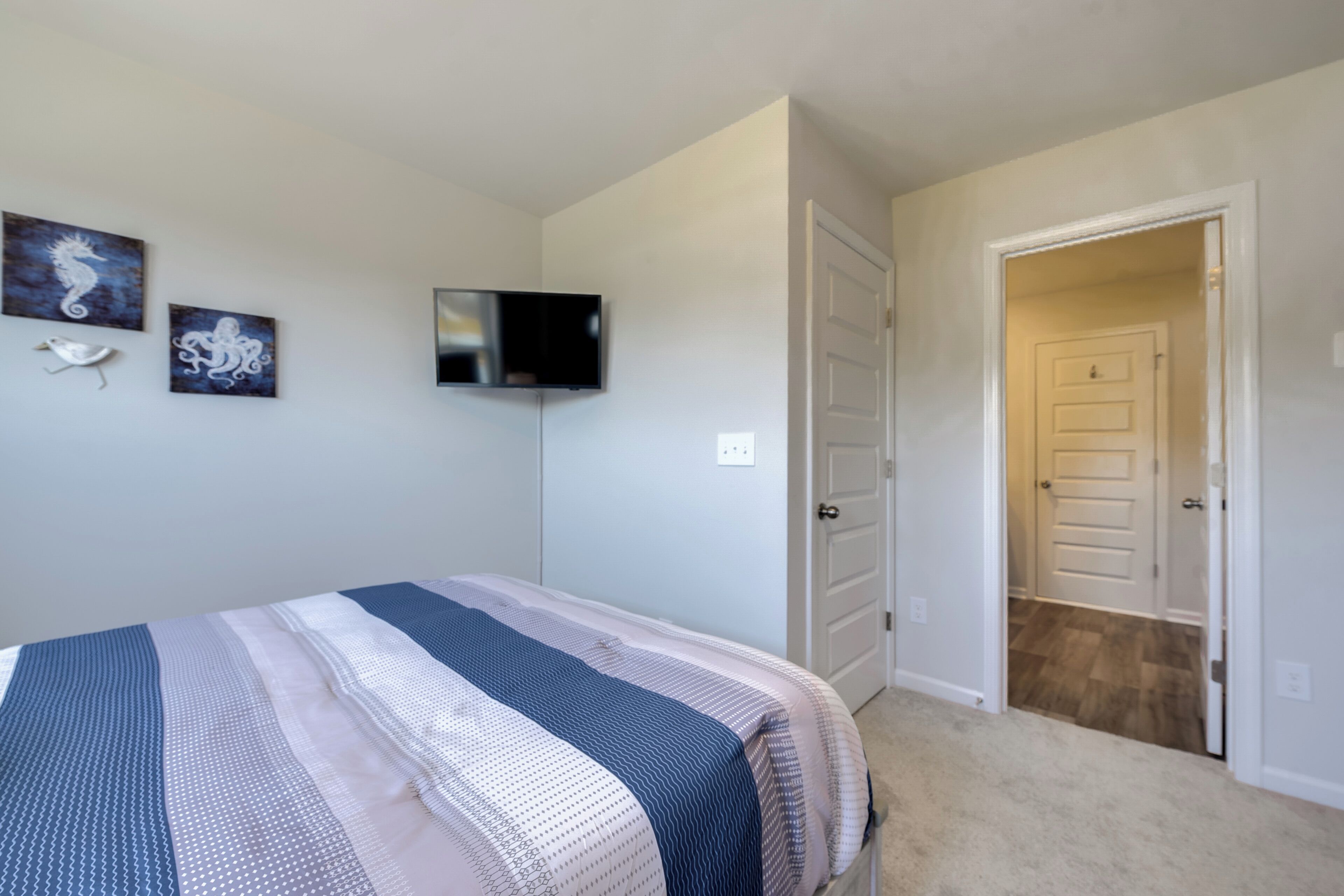 A bedroom with a bed, a flat-screen TV, and two wall-mounted artworks.