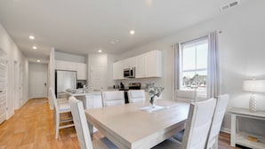 A modern kitchen with white cabinetry, a dining table with chairs, and a view through a window. - 2 Mi to Ocean Isle Beach! Coastal Getaway w/ Patio (Ocean Isle Beach)