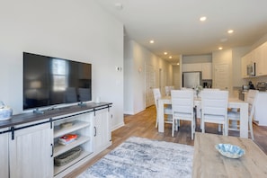 A modern kitchen with white cabinets, a large flat-screen TV, and a dining area with white chairs.