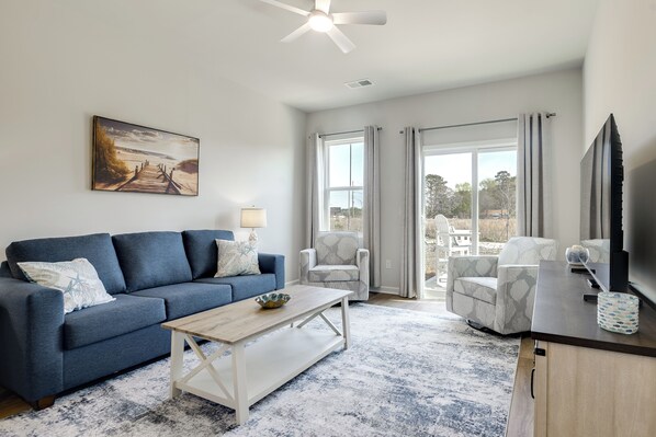 A living room with a sofa, coffee table, and armchairs, a painting on the wall, and a large window with curtains.