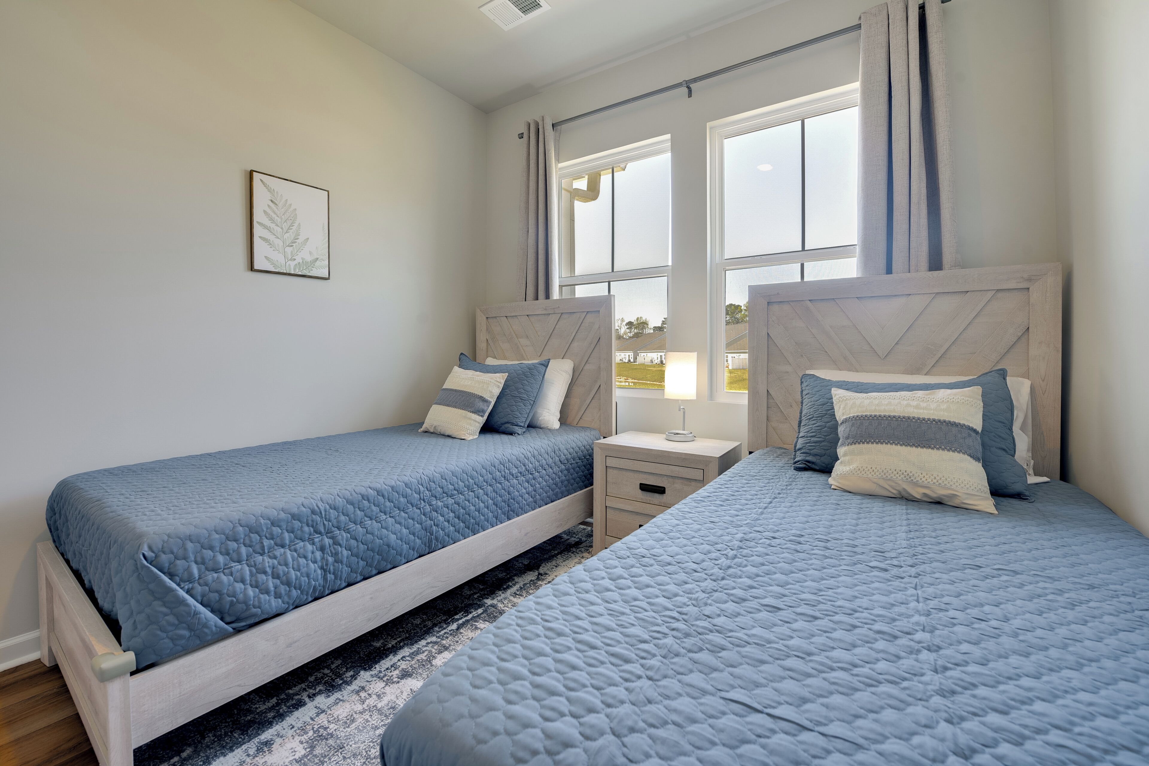 A bedroom with two beds, a nightstand, and a window with curtains.