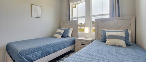 A bedroom with two beds, a nightstand, and a window with curtains.