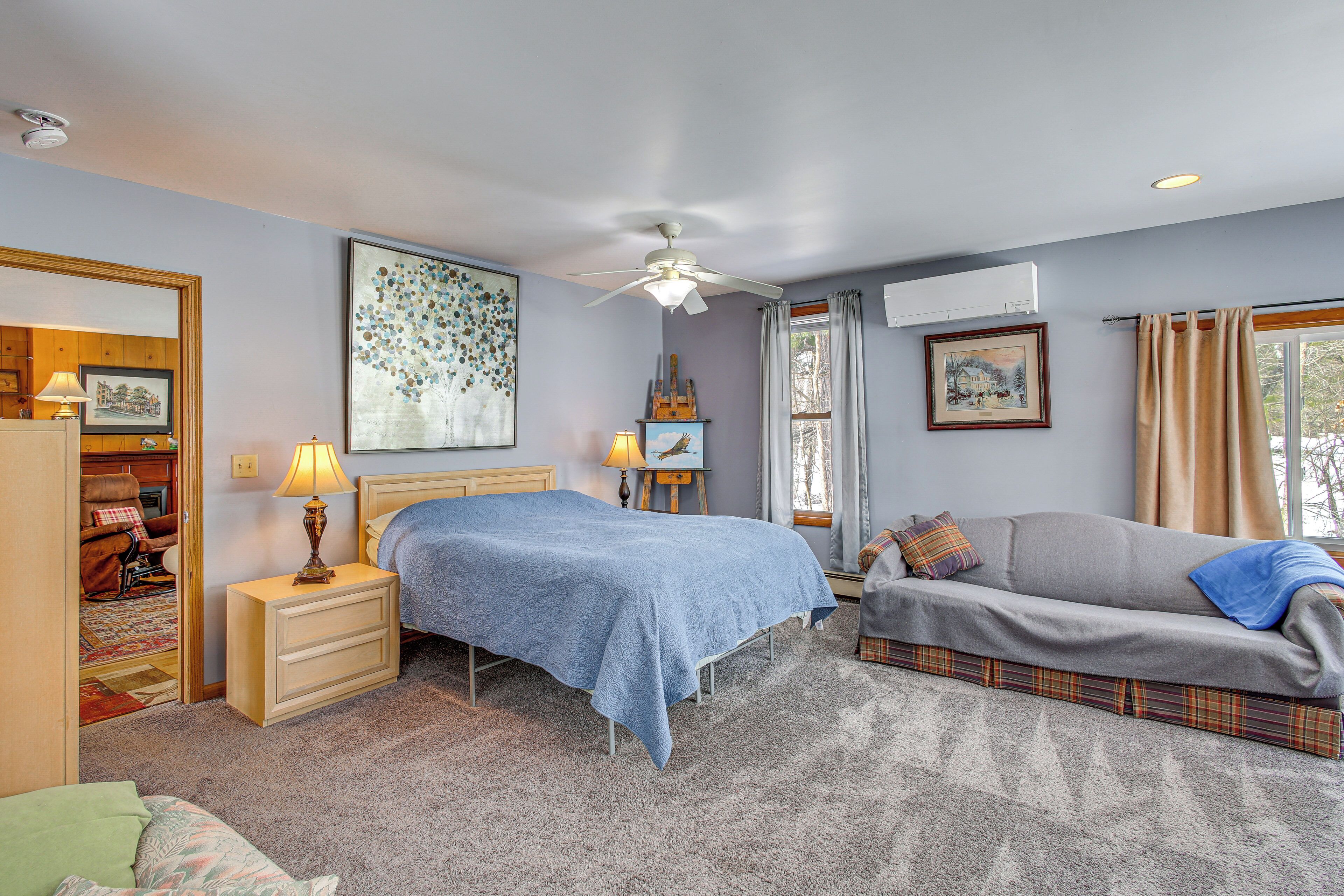 A bedroom with a bed, a sofa, a nightstand, a lamp, and a ceiling fan.