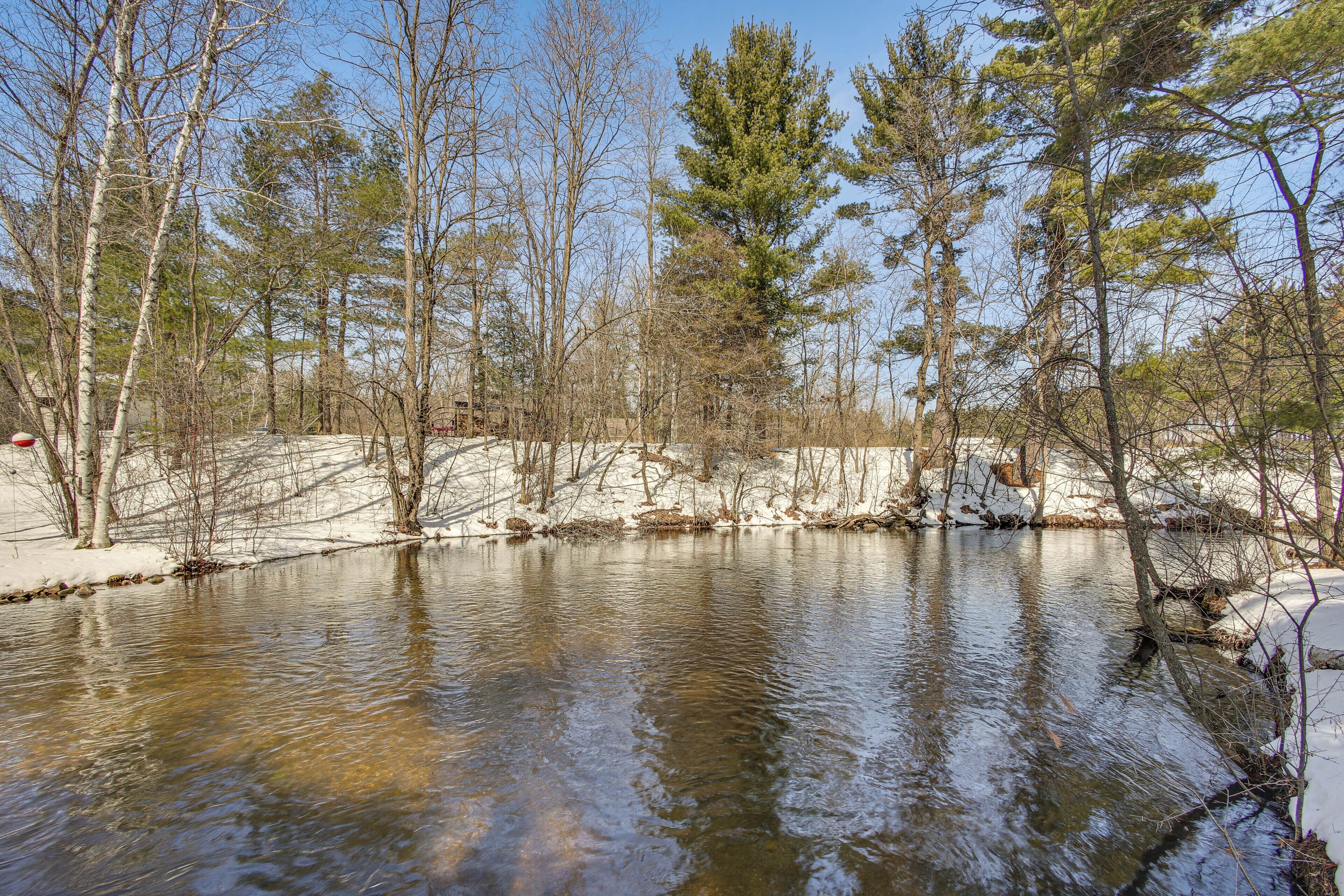 A natural landscape with a body of water, trees, and snow-covered ground.