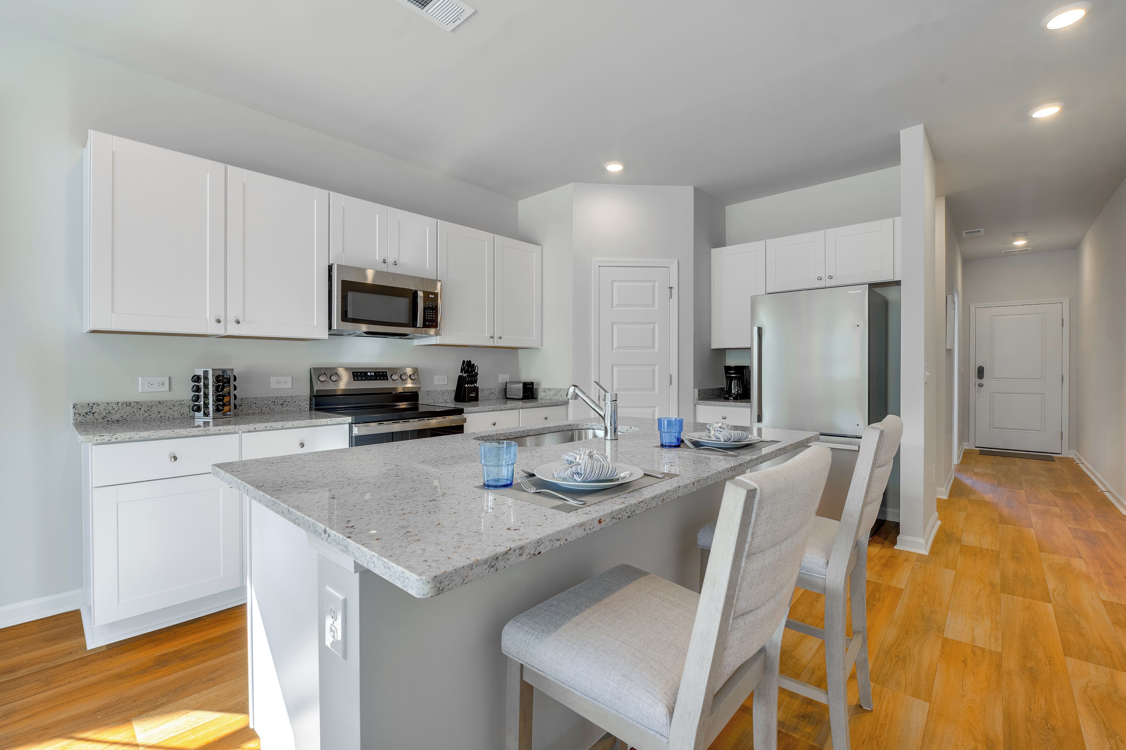A modern kitchen with white cabinets, a granite countertop, stainless steel appliances, and a central island with bar seating.
