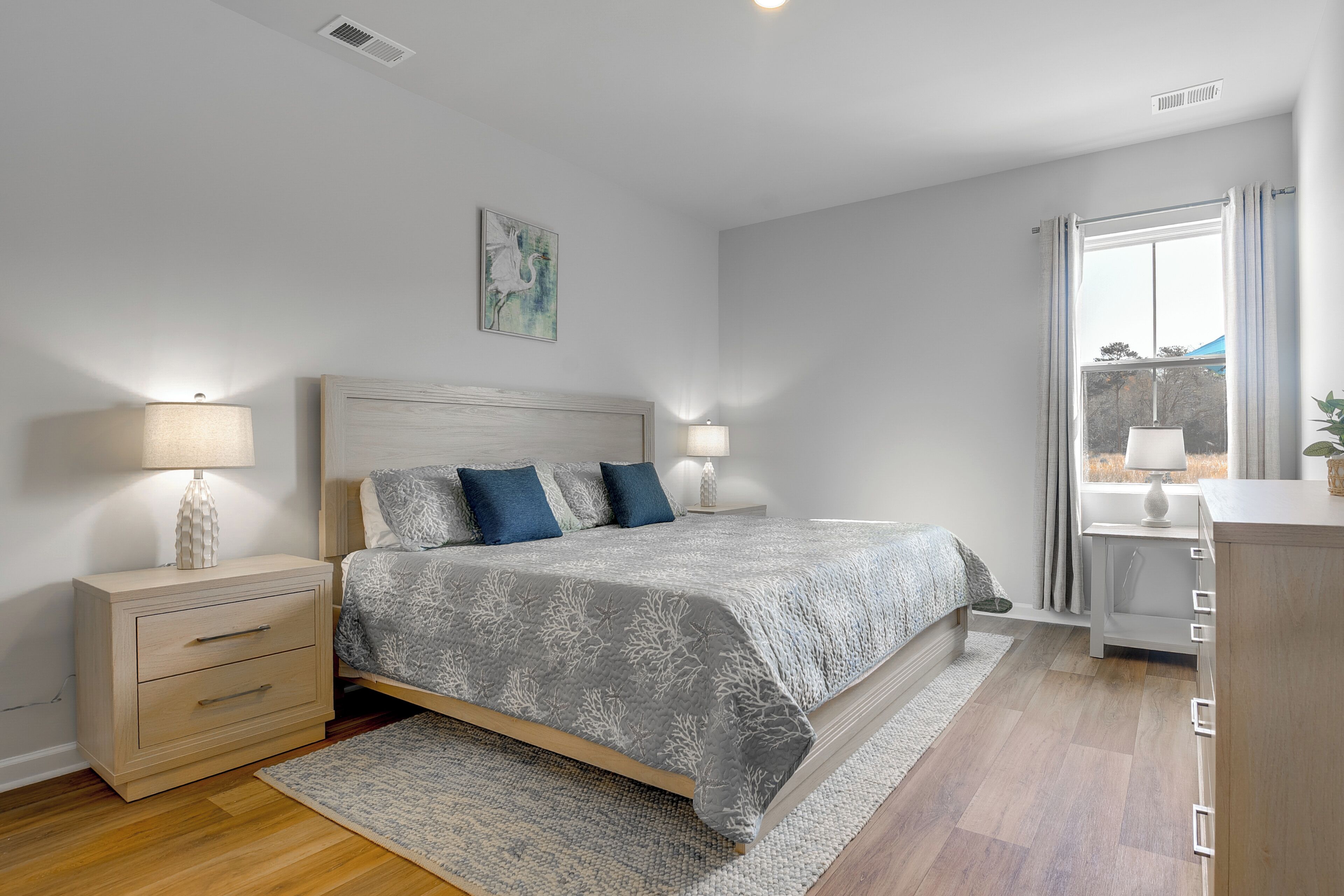 Une chambre à coucher avec un lit, des tables de chevet, une fenêtre avec des rideaux et un tableau au mur.