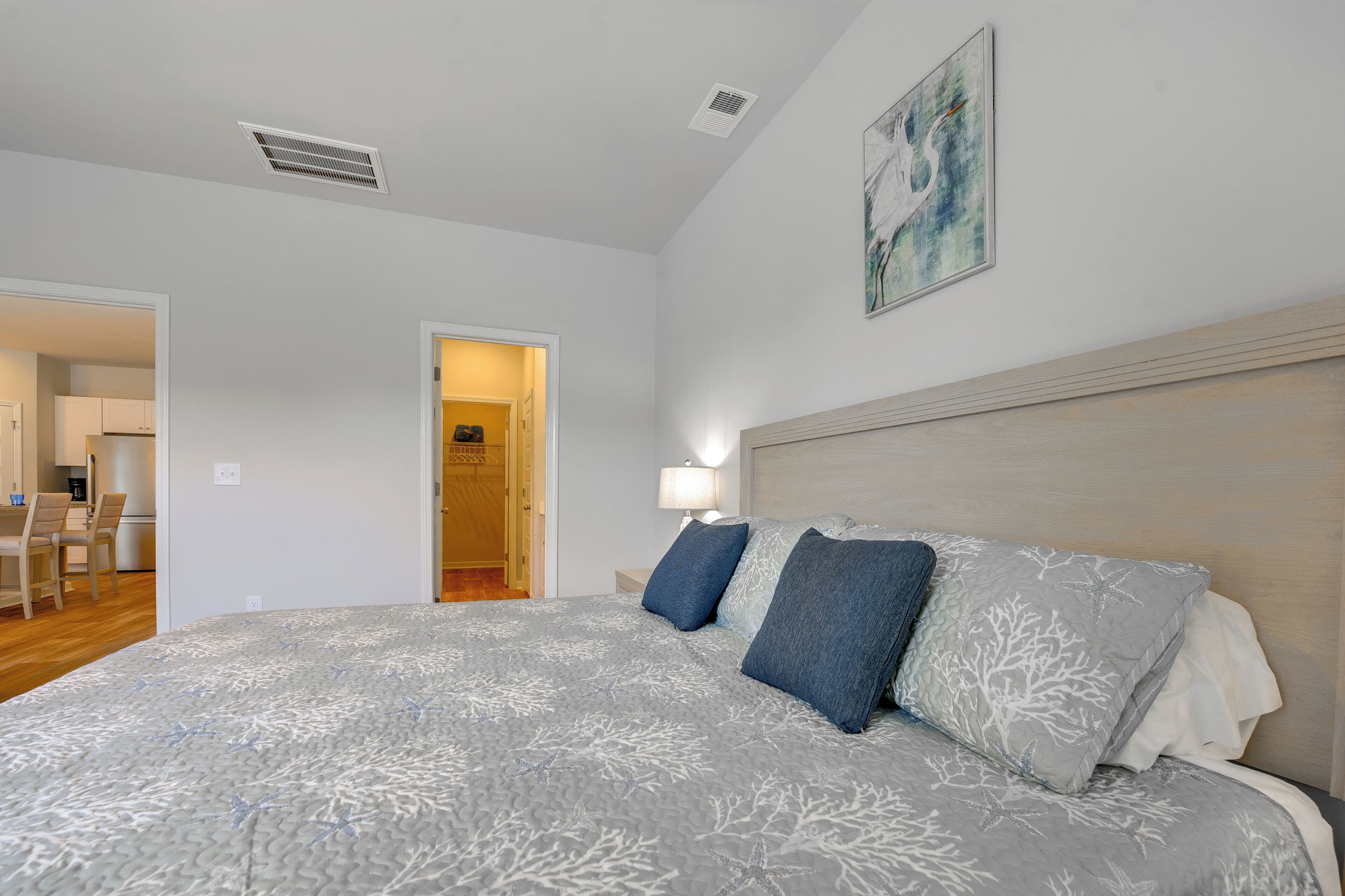 A bedroom with a bed, a headboard, a nightstand, a lamp, and a door leading to a bathroom.