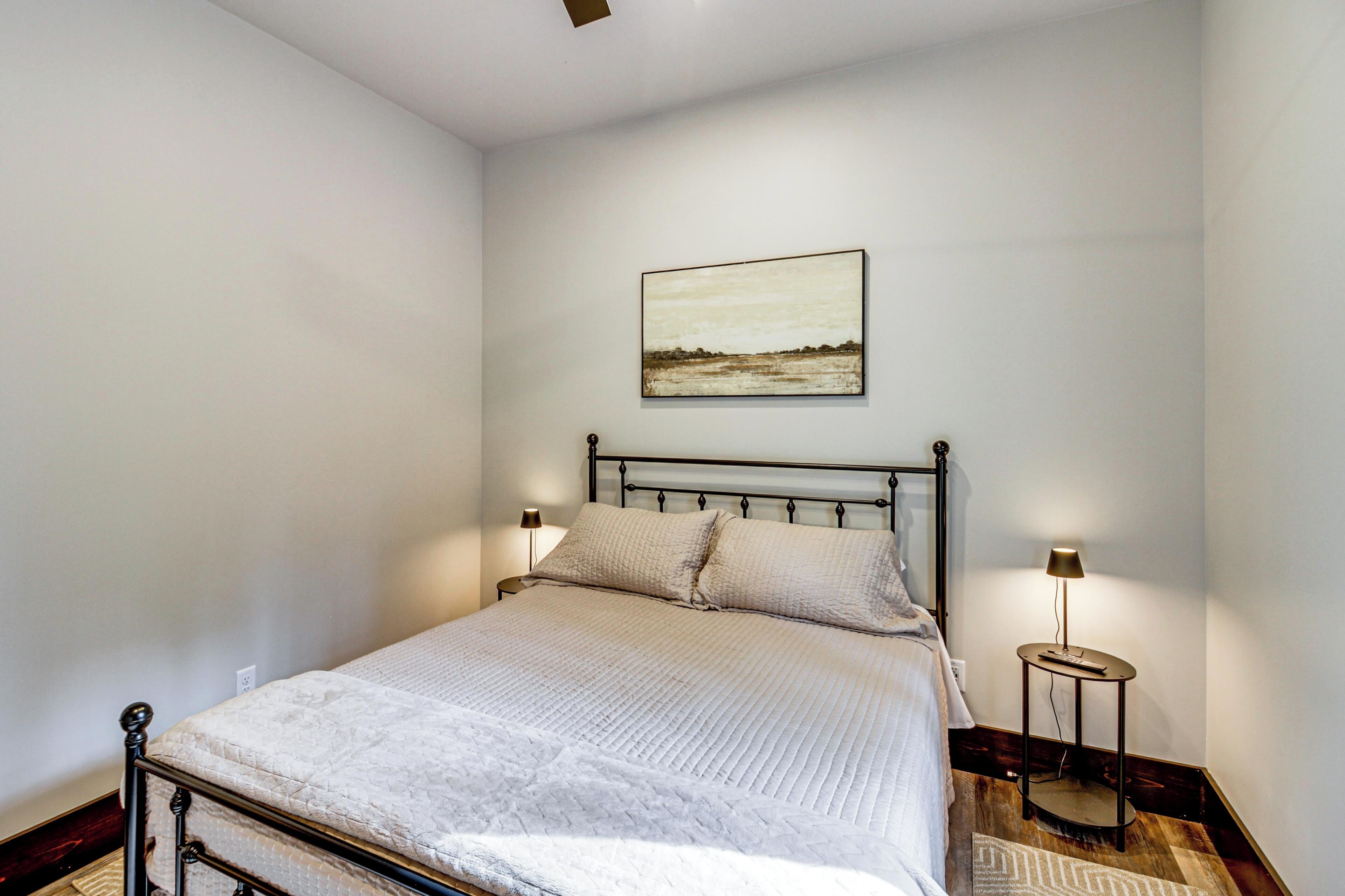 A bedroom with a bed, bedside lamps, a painting on the wall, and a small table.