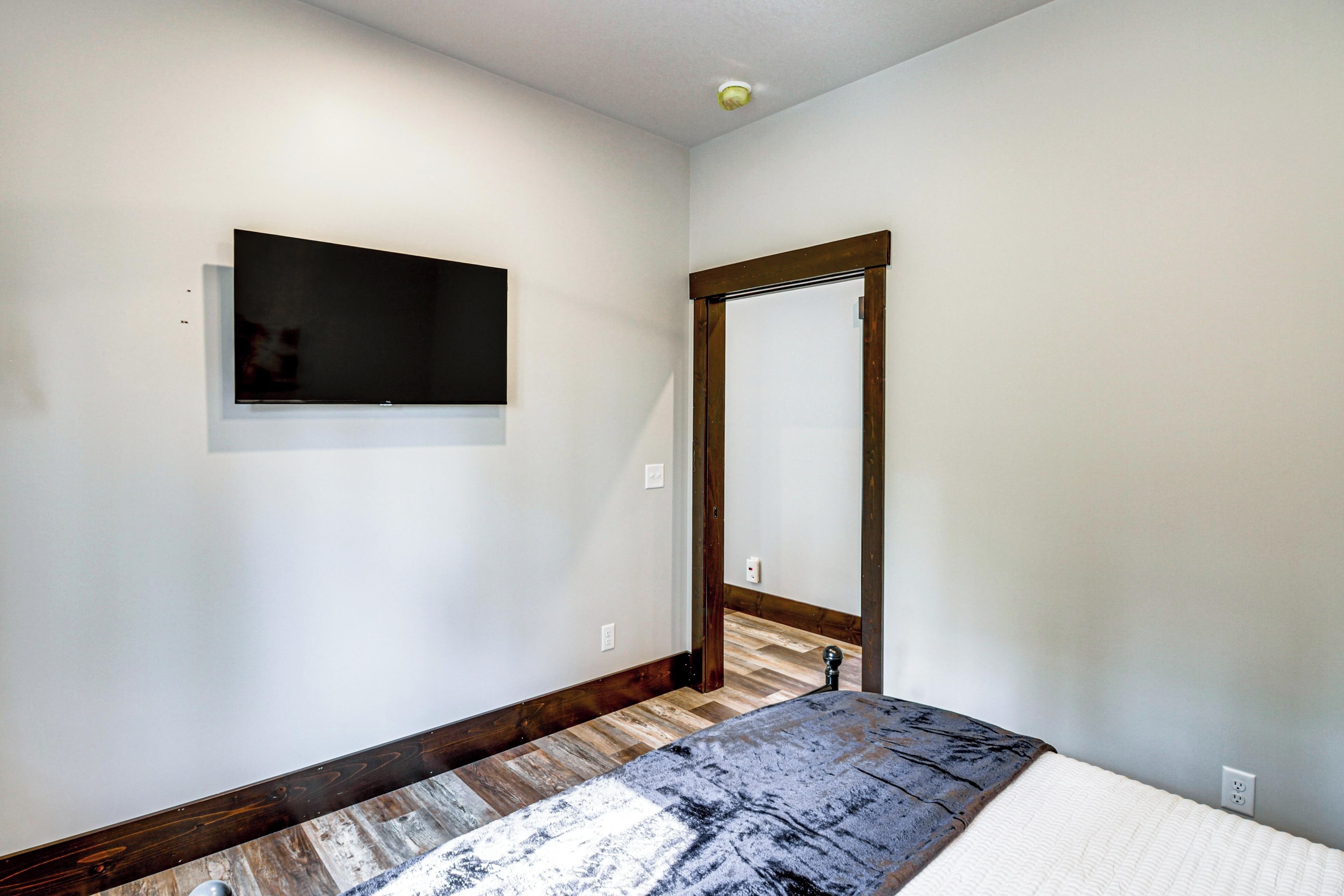 Een slaapkamer met een bed, een flatscreen televisie aan de muur, een houten deur en een parketvloer.