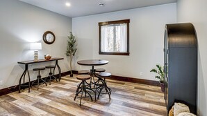 A room with a wooden floor, a round table with stools, a wall clock, a window with curtains, and a black cabinet. - 4 Mi to Golf: Family Home in Nisswa, Near Lakes! (Nisswa)